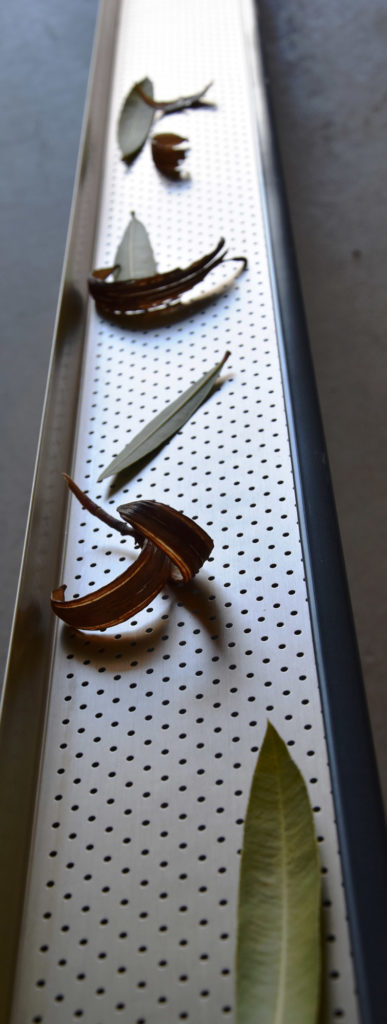Grille pares-feuilles installée dans une gouttière pour montrer qu'elle permet de retenir les feuilles sans empêcher l'évacuation de l'eau